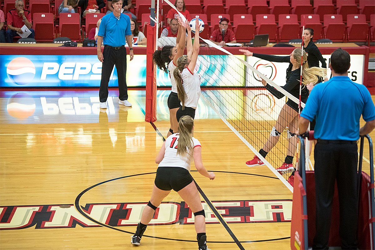 volleyball players blocking a ball at the net