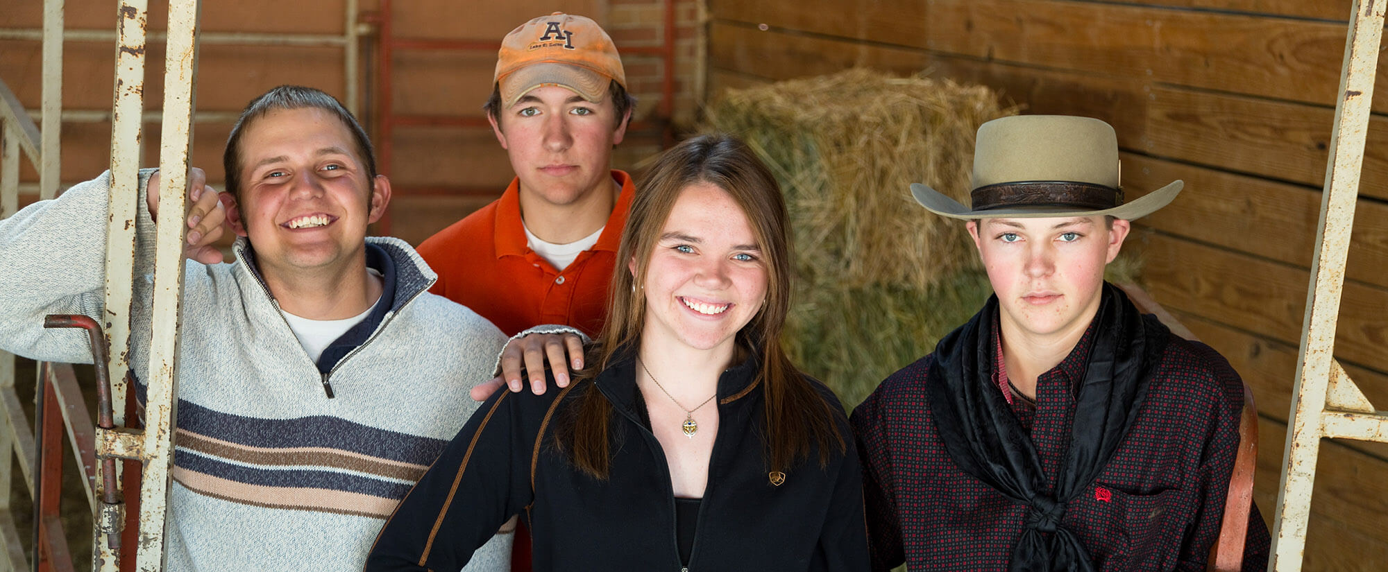 Four young students looking toward the camera, standing in a barn.