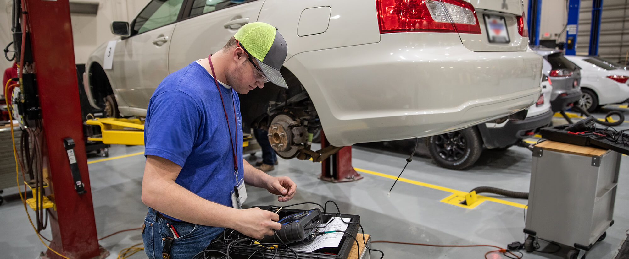 Photo of college student working on a small computer attached to a car that is on jacks.