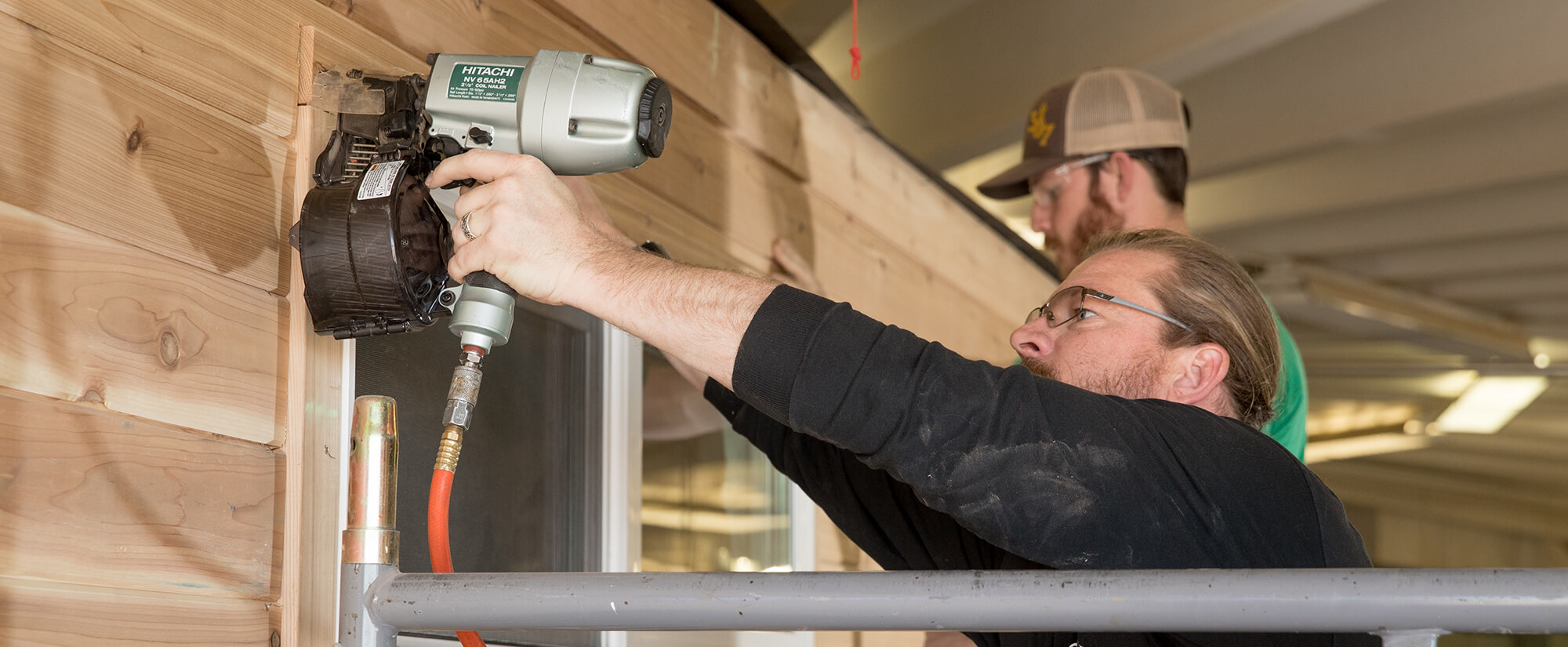 A student uses a nail gun to frame a window of a tiny home.