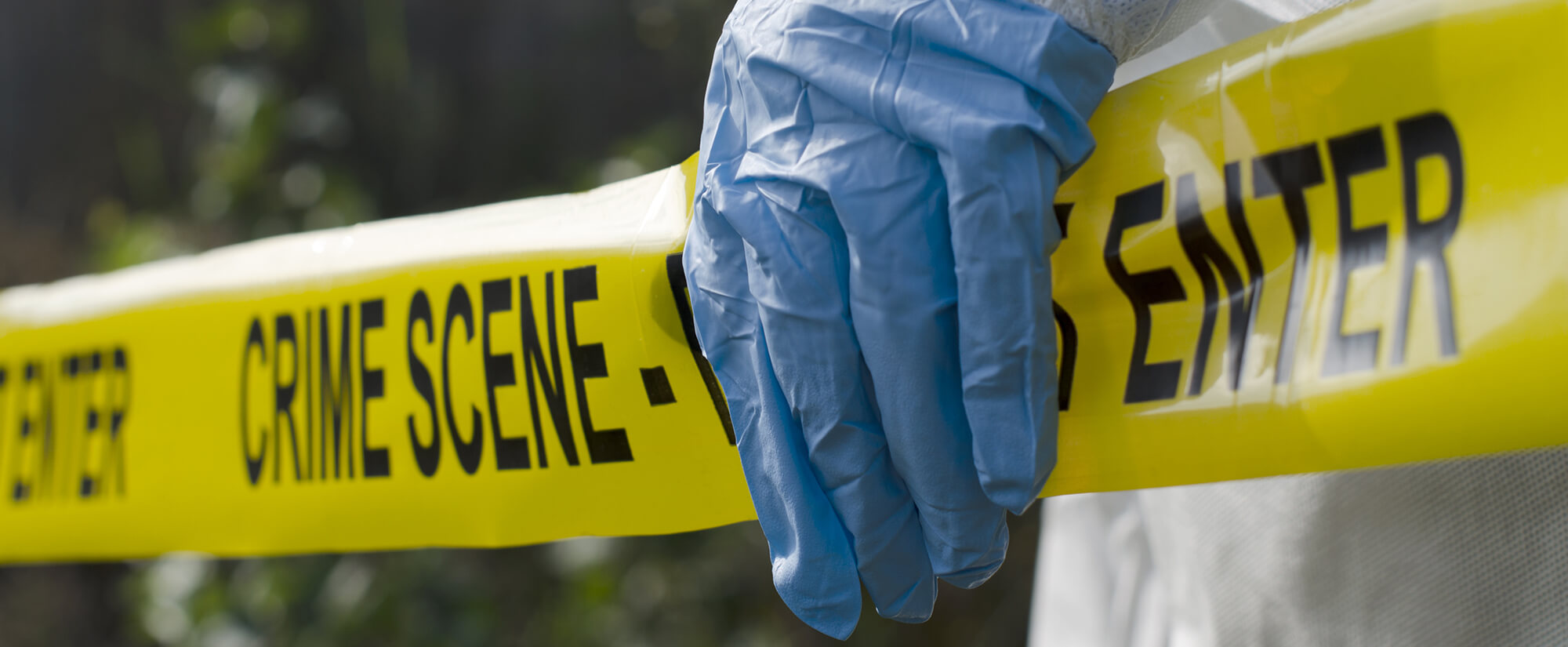Photo of a gloved hand holding up a section of yellow crime scene tape.