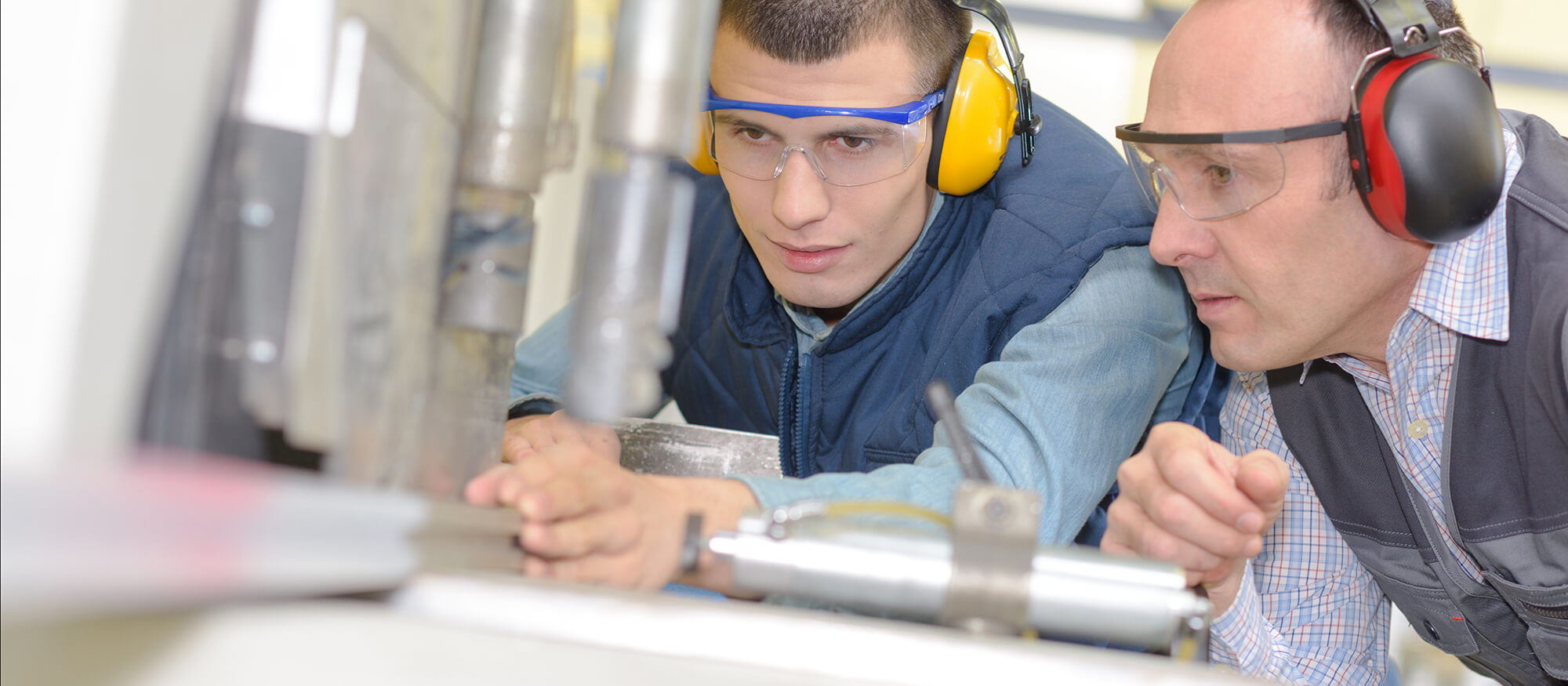 Photo of instructor overseeing a student work with a lathe.