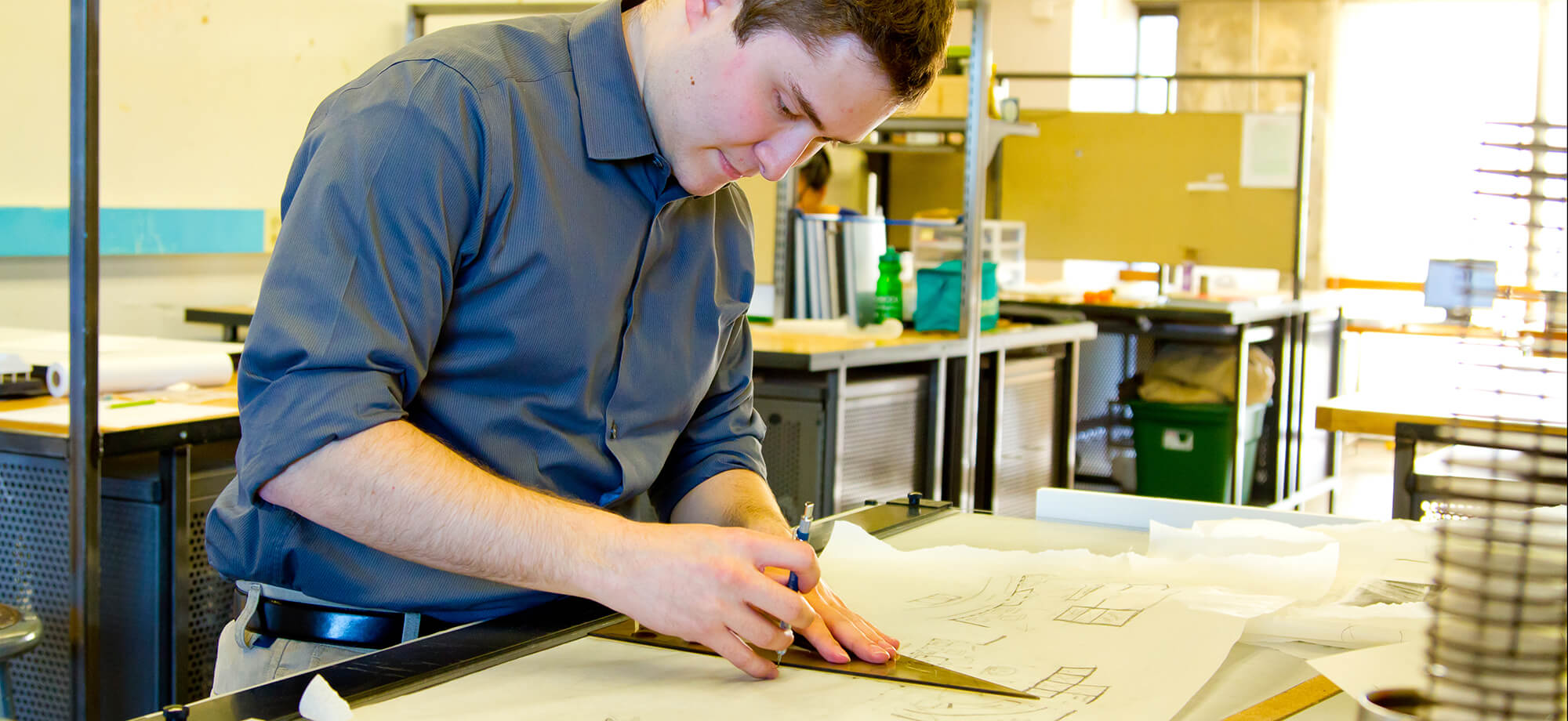 Photo of a young man working on construction plans in a workshop.