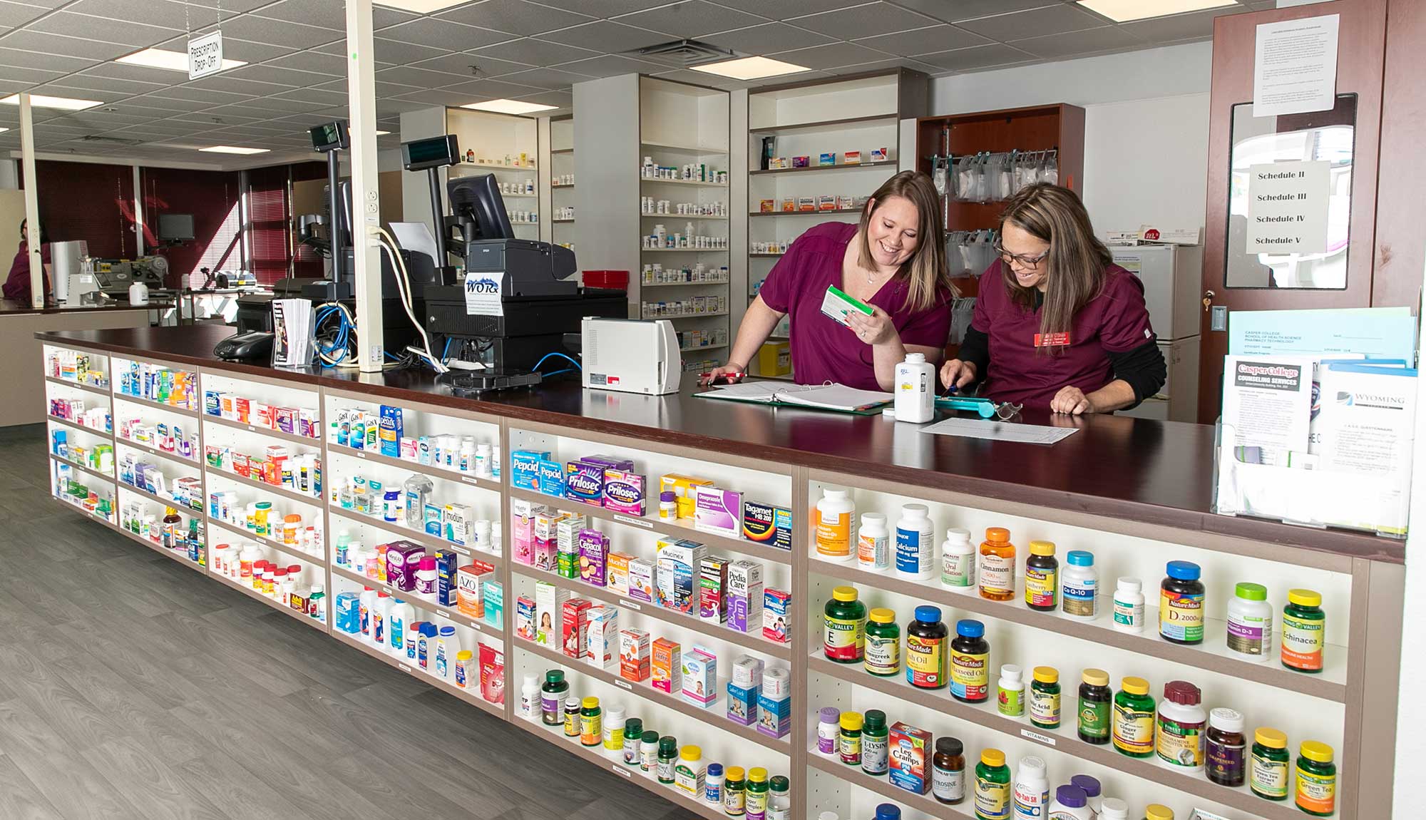 A student holds a pill bottle while walking past shelves set up like a pharmacy.