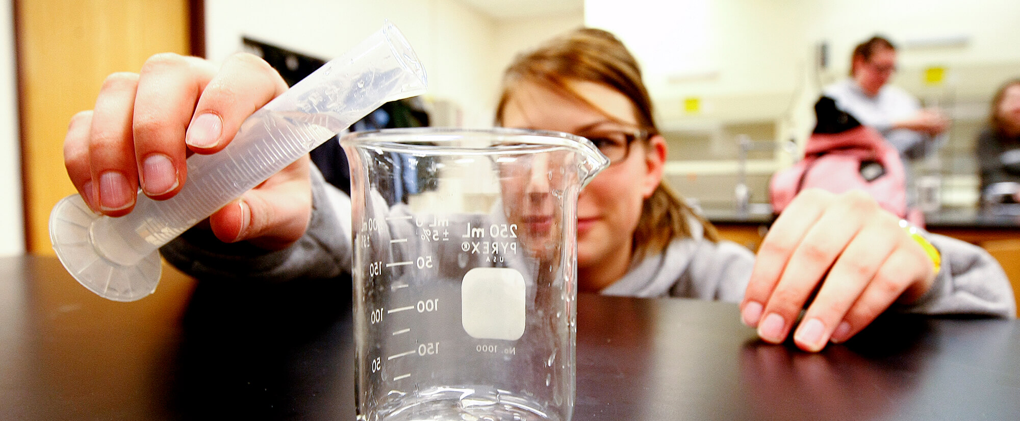 A student pours a liquid from a small measuring tool into a measuring cup.