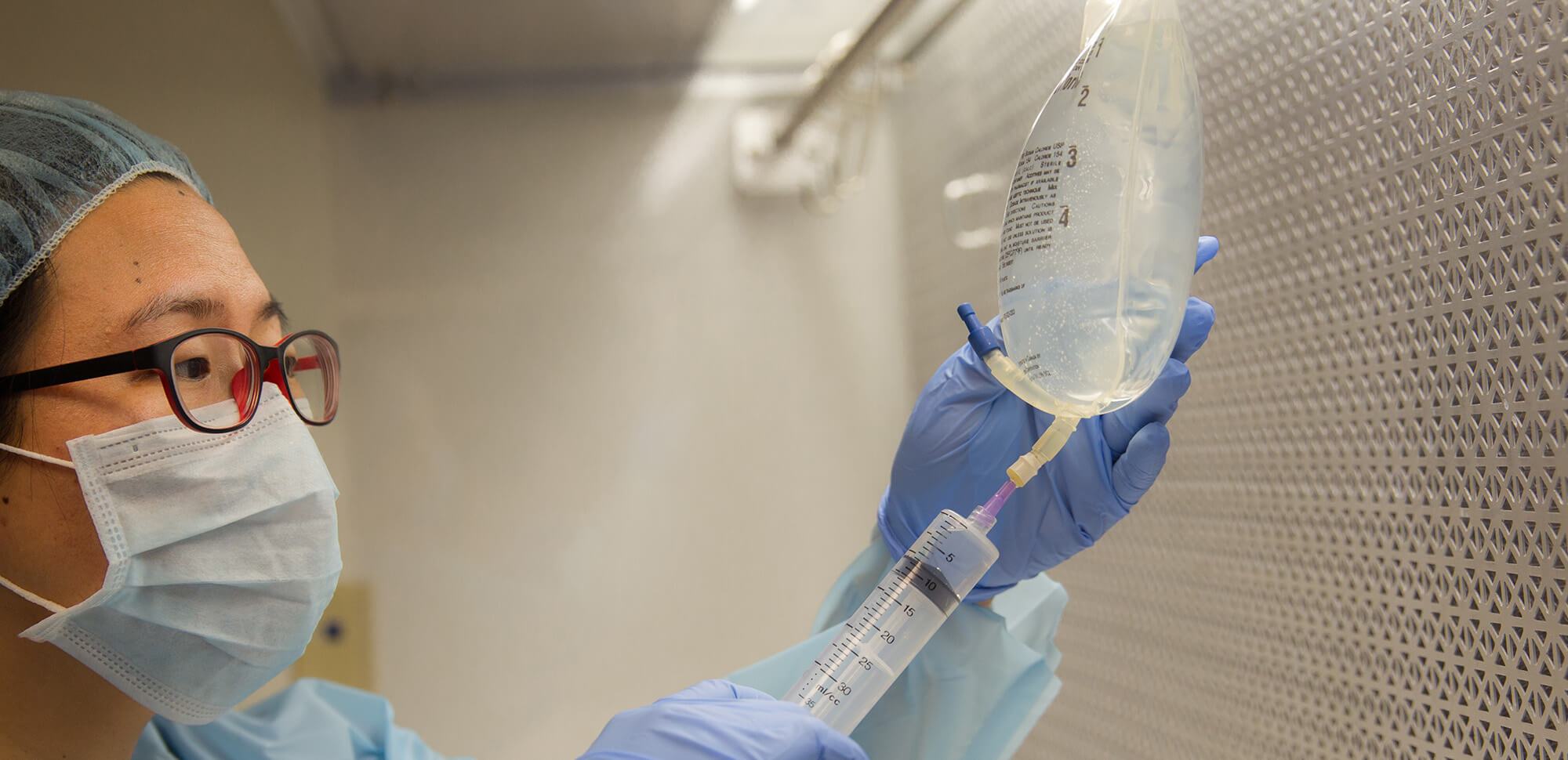 A medical professional connects a syringe to a bag filled with fluid.