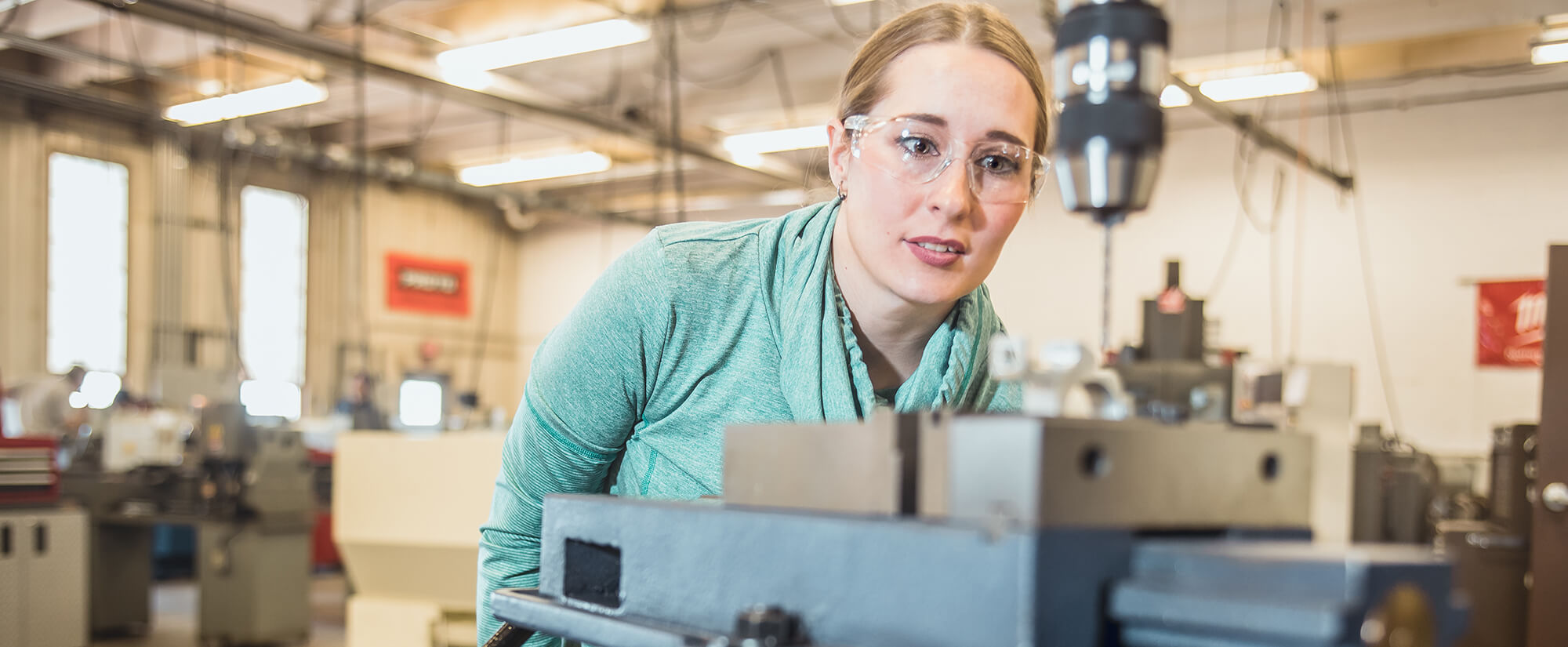 A female student wearing safety glasses in a machine tool classroom.