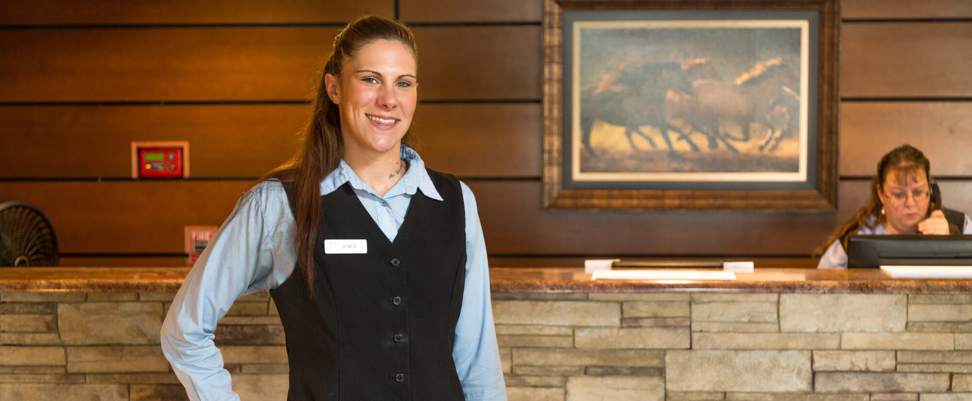 Hotel manager standing in front of a hotel desk staffed by an employee answering the phone. Hospitality and tourism management