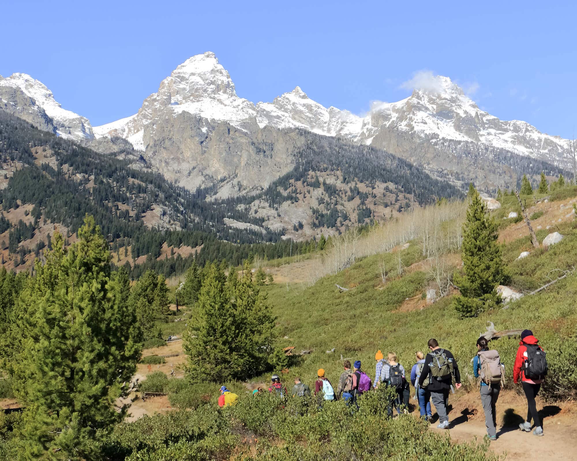 students hiking on a trail with Teton mountains in the distance