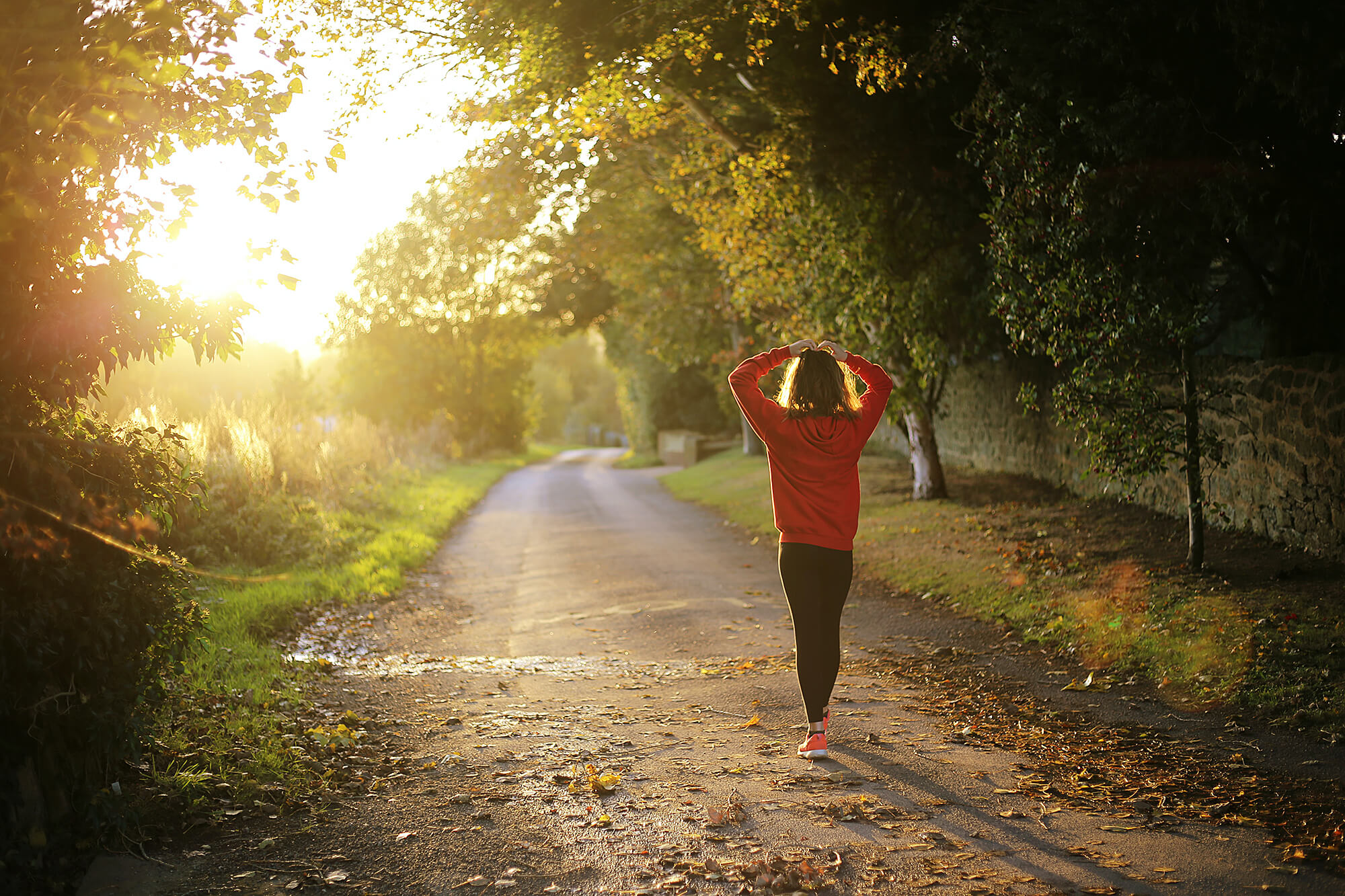 Photo of a woman walking on a dirt road at sunset.