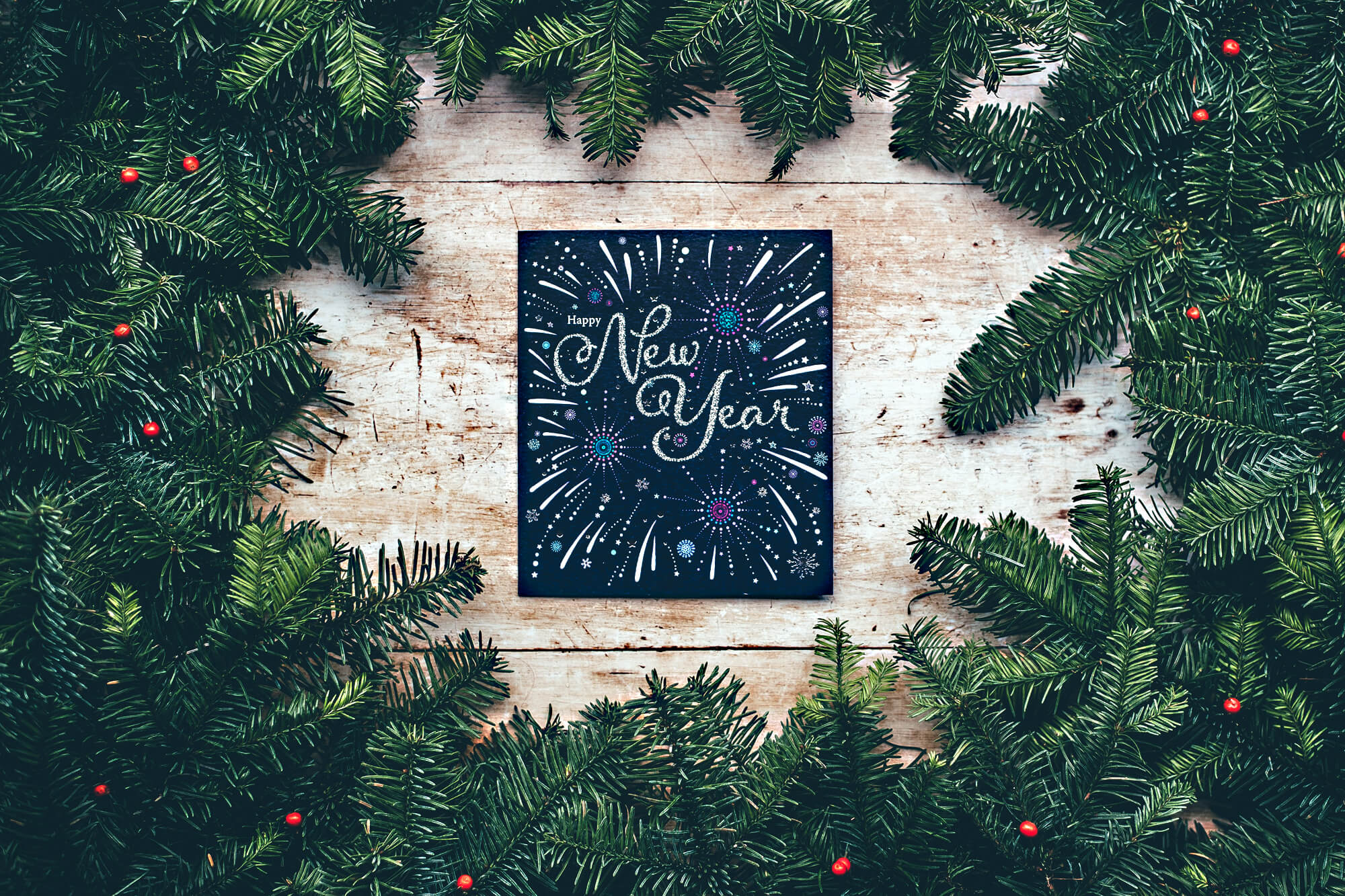 Photo of pine boughs with a sign in the middle that reads "Happy New Year."