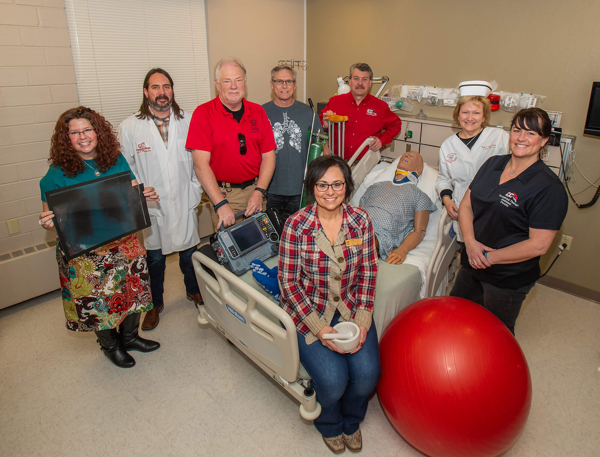 a group of instructors pose with object representing each of their respective programs.