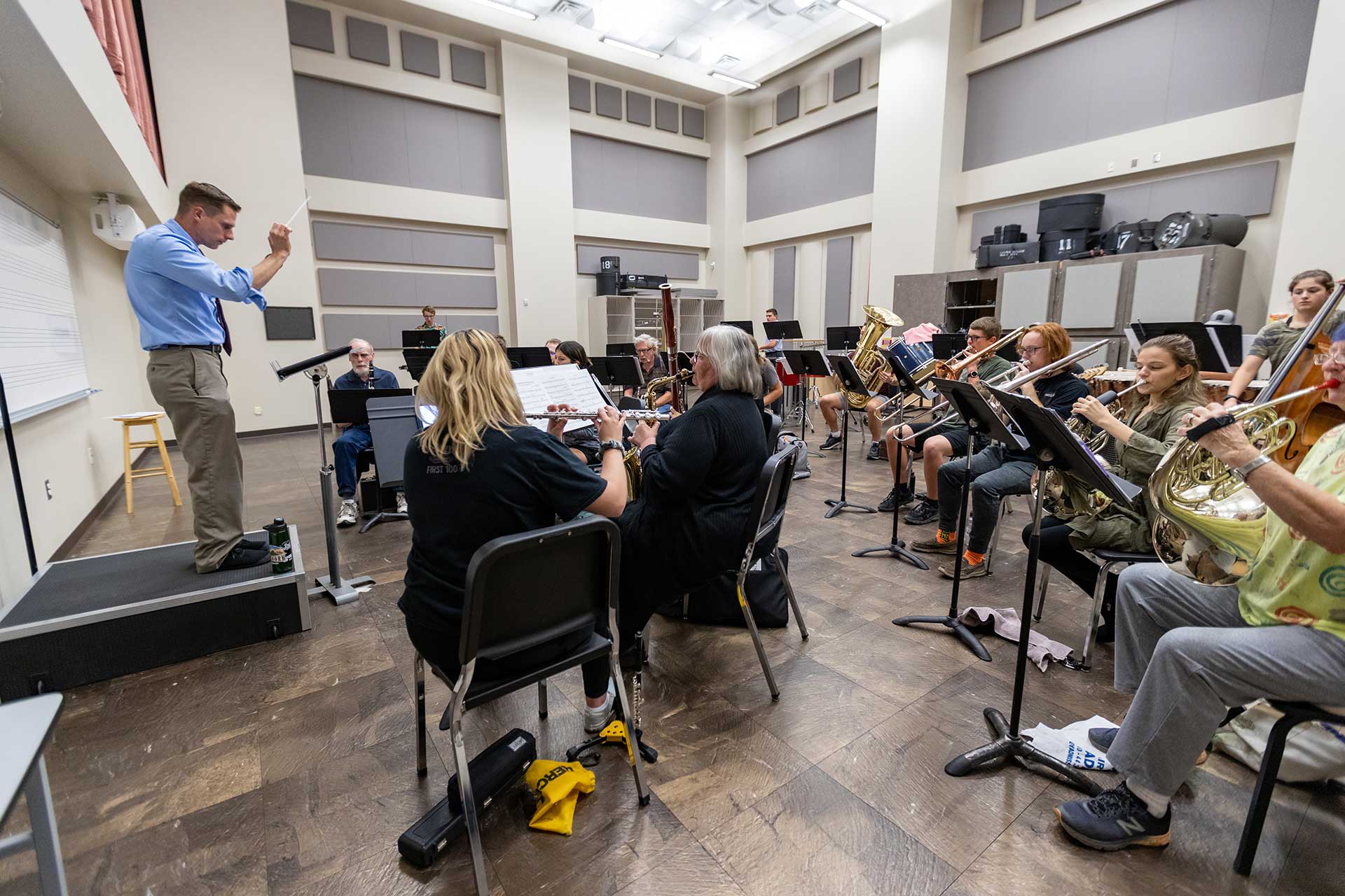 Students practice vocal exercises while gather around an instructor playing the piano.