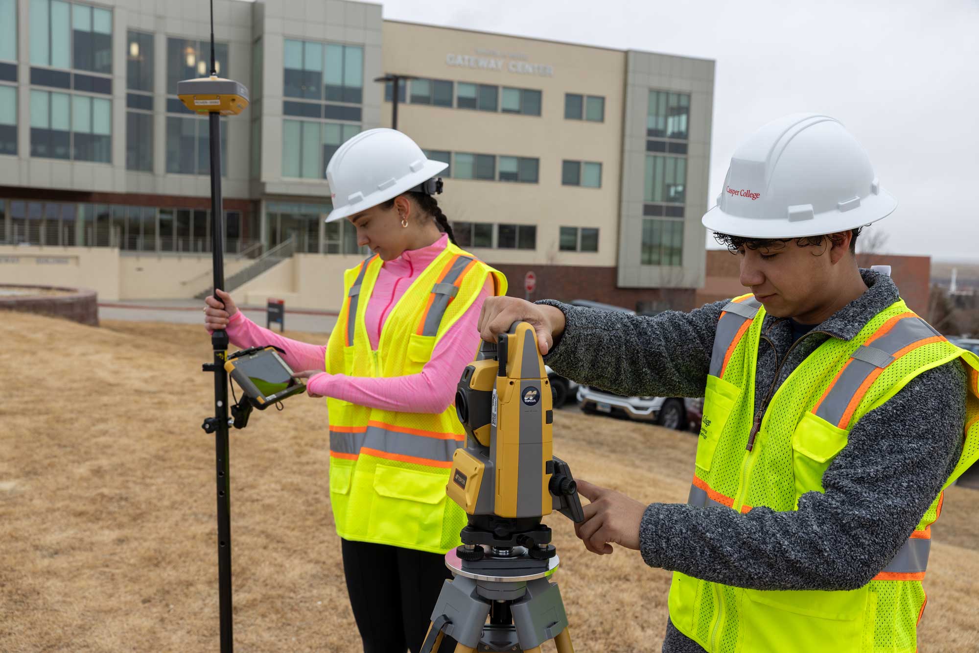 Students looking at blueprints with construction materials in the background including wood and a hammer.