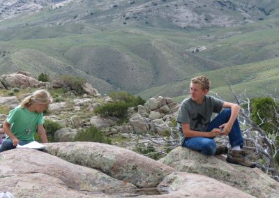 two students sitting on rocks overlooking a grassy hillside