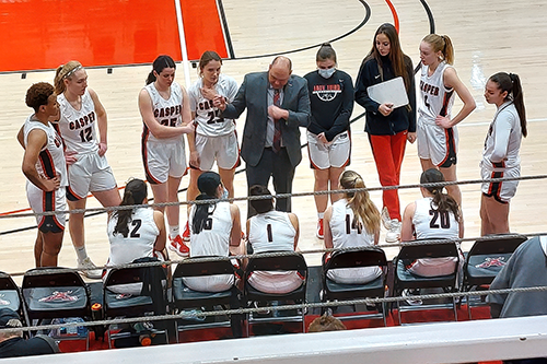 Photo of Assistant Women's Basketball Coach Nate Macy with the 2022-2023 team discussing strategy.