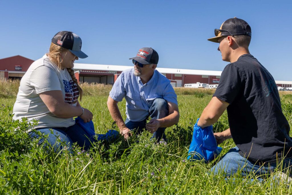 Agriculture instructor and students examine forage plants during an outdoor field identification activity.