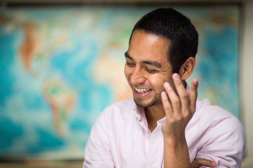 International Studies instructor laughs during a conversation with a world map displayed in the background.