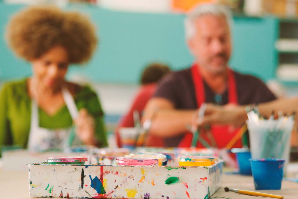 Blurred foreground of children painting with jars of colorful paint in a classroom of art education.