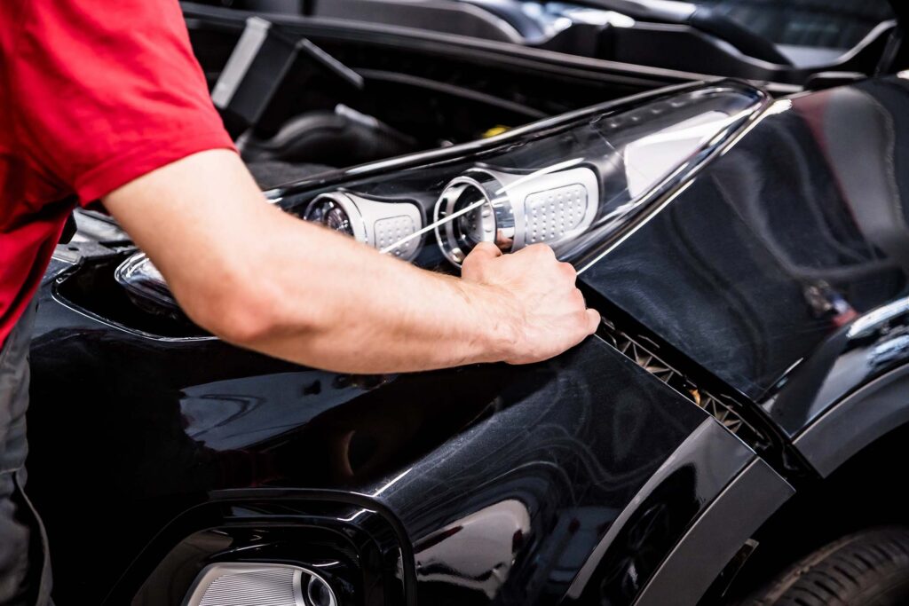 Close-up of a person polishing or repairing a black car panel. Auto Body Repair Technology
