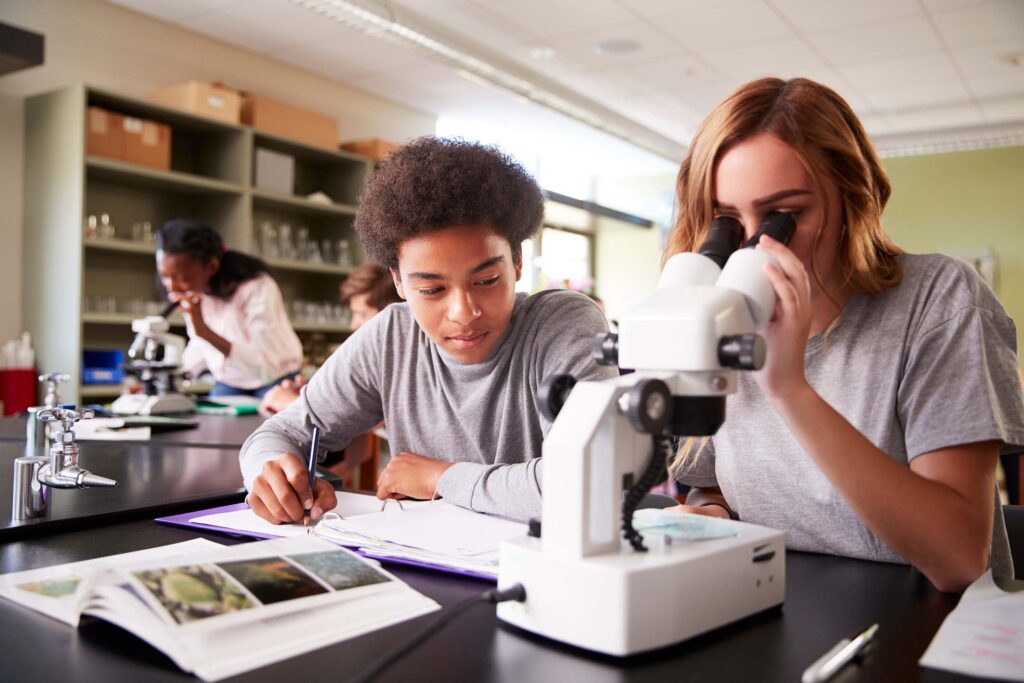 Two students in a lab looking through a microscope together studying biology.