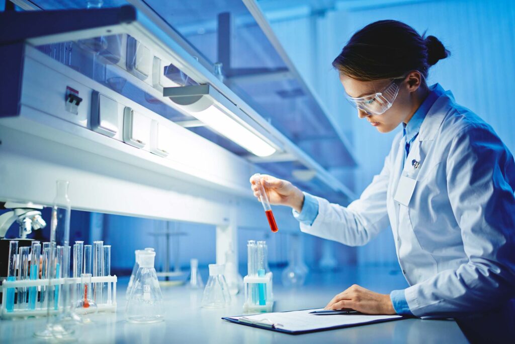 Scientist in a lab coat working with test tubes under bright laboratory lighting doing chemistry.