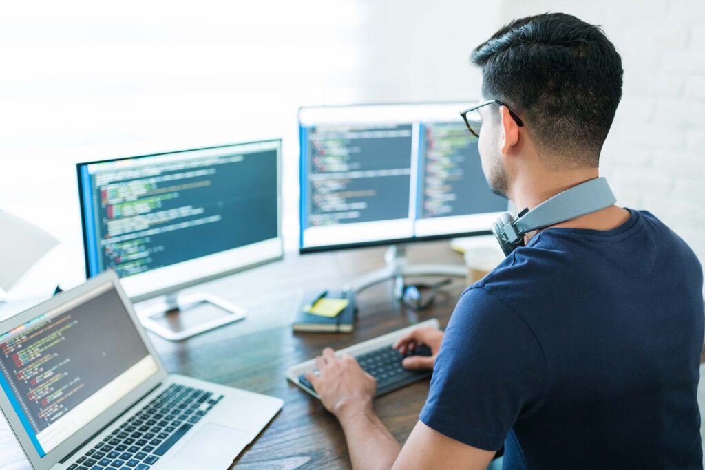 Student working at a computer with code displayed on multiple screens for his computer science class.