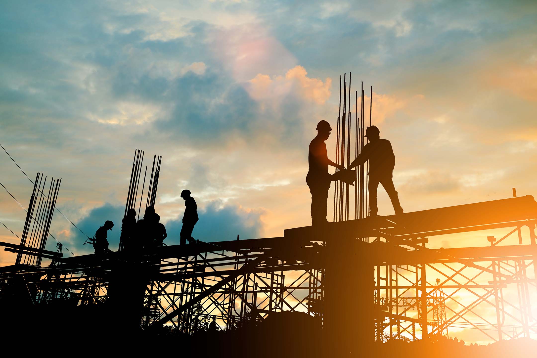 Silhouetted construction workers standing on a steel structure at sunset. Construction management