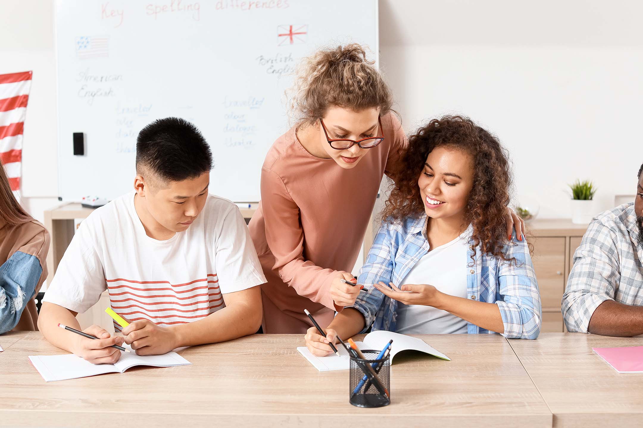 English teacher helping students with writing at a classroom table.