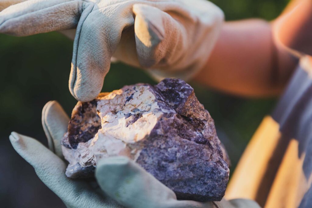 Gloved hands holding and examining a rock sample outdoors. Geology
