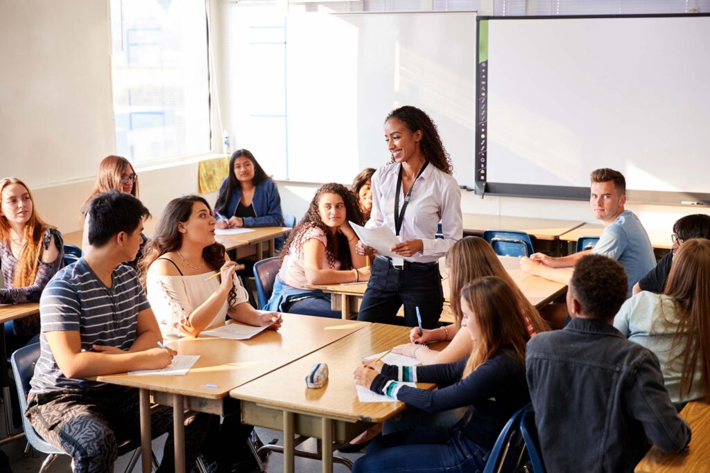 Spanish instructor speaking to a classroom of students gathered around tables.