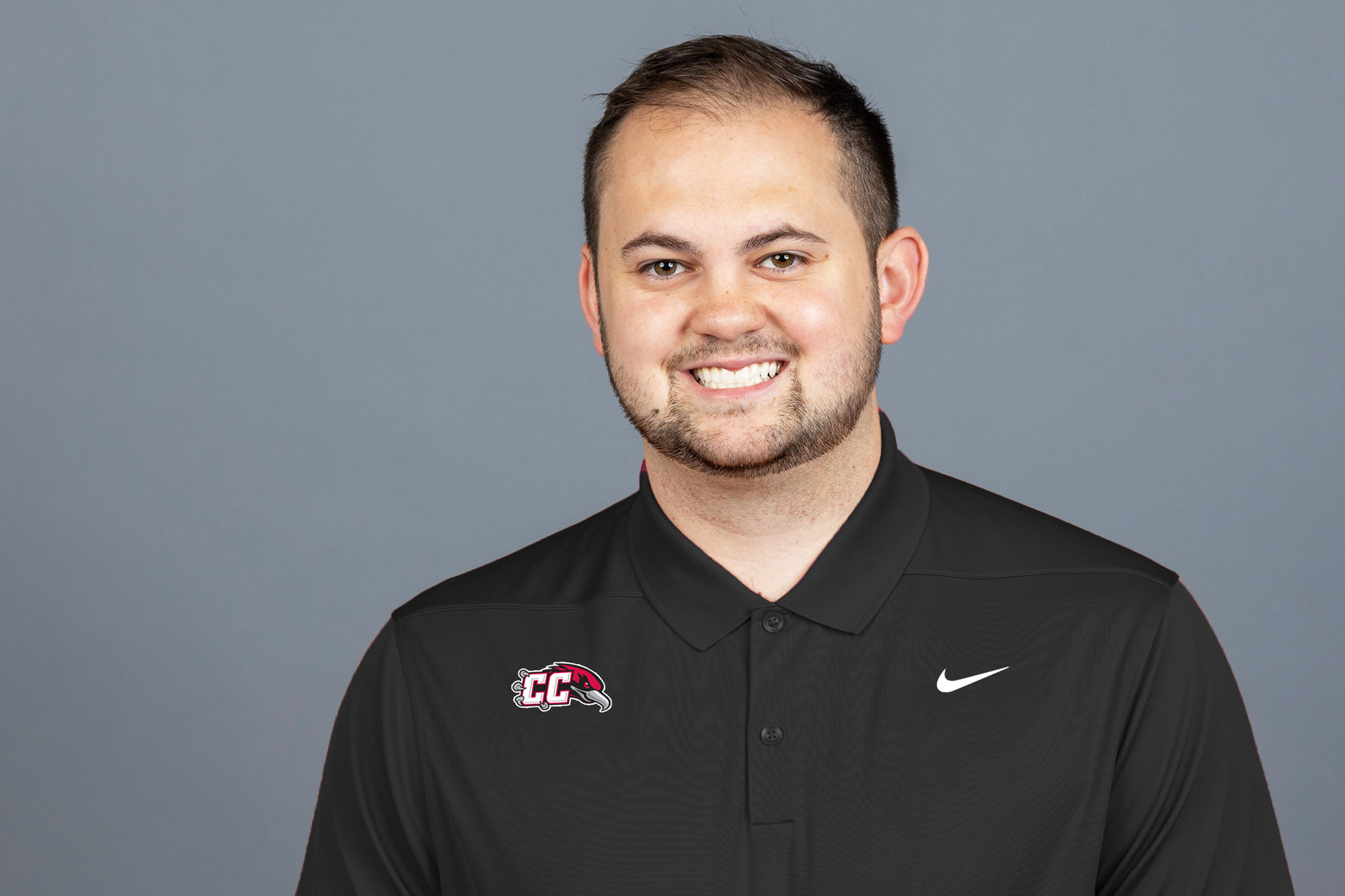 Headshot of Ty Larson, the new Casper College Men’s Basketball Head Coach, wearing a black Nike polo with the CC Thunderbirds logo.