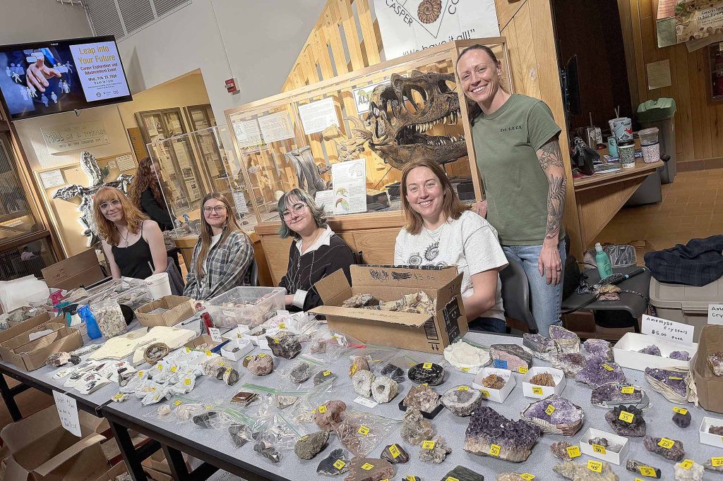 Five Casper College students standing behind a table covered in various mineral and crystal samples at the Tate Museum.