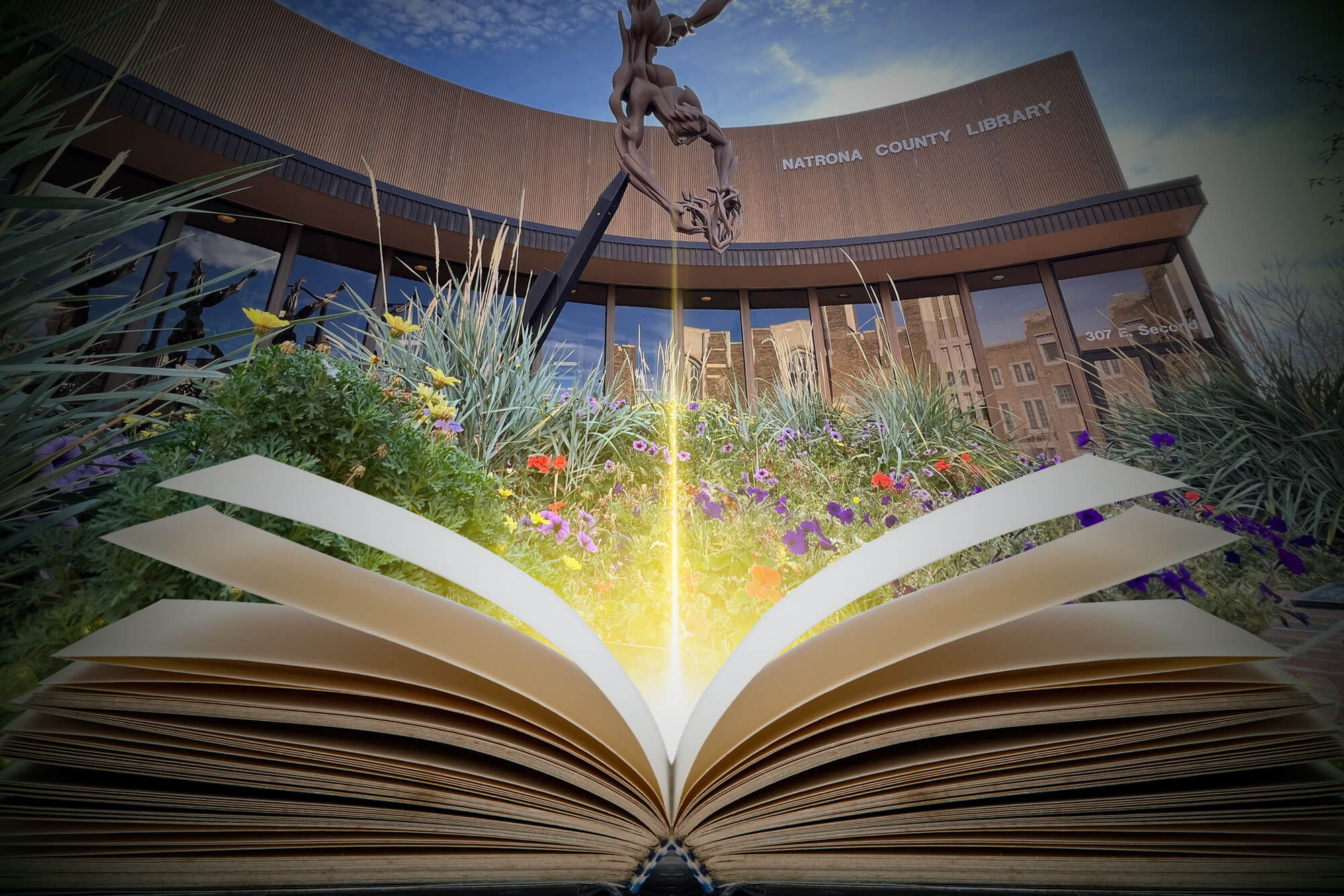 casper-college-big-read-partnership-image An open book with glowing light emanating from its pages in front of the Natrona County Library building and its "The Oracle" sculpture.