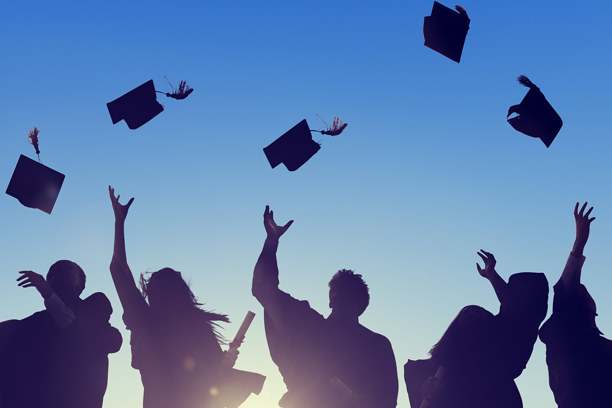 Silhouette of graduates throwing caps in the air against a blue sky.