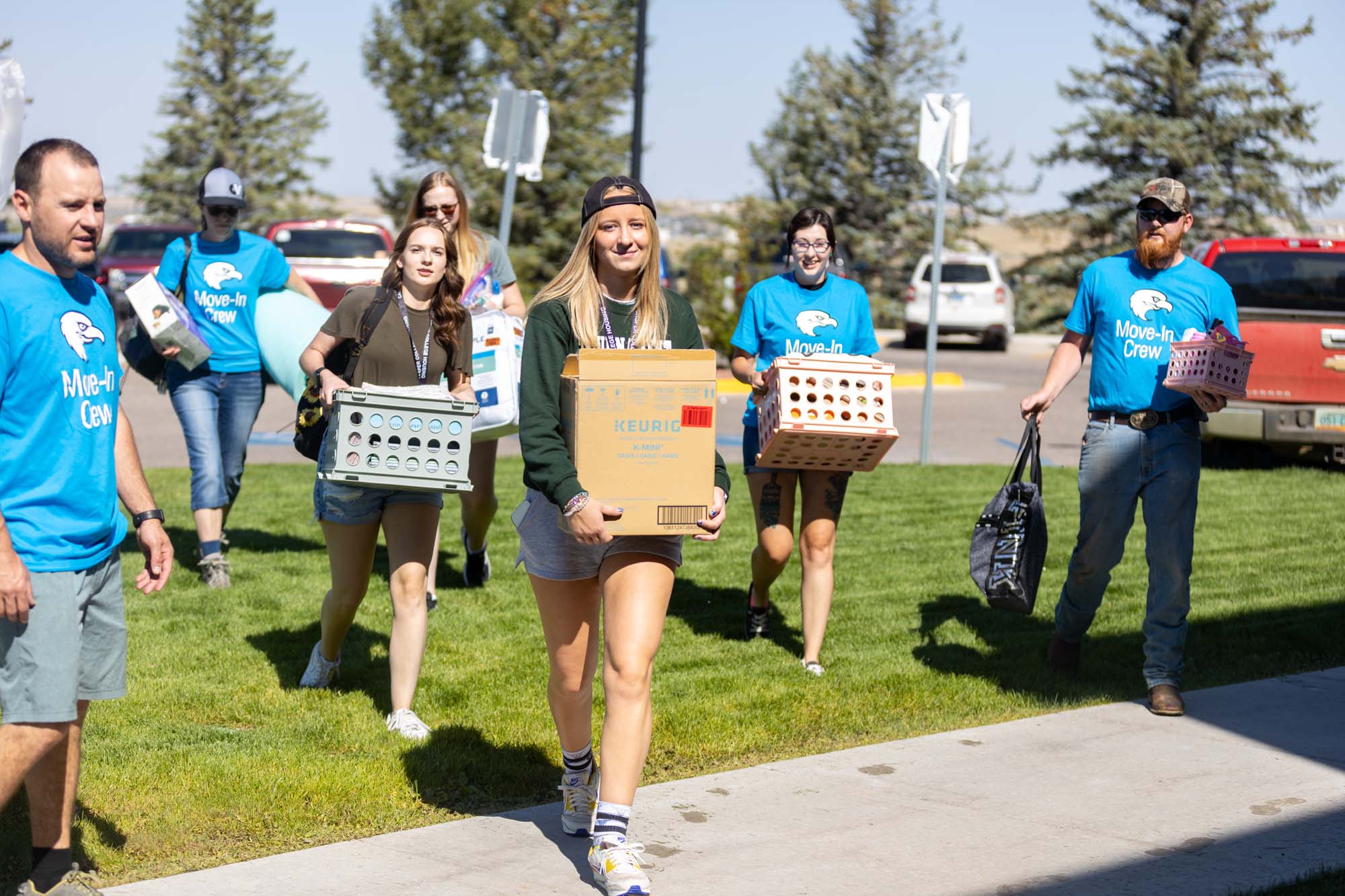 A female student smiling and carrying a large cardboard box into a residence hall during Casper College Move-In Day.