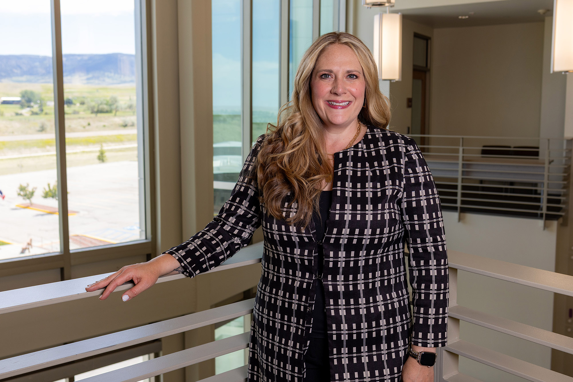 alicia-roberts-human-resources-image-0626 Alicia Roberts, the new human resources director at Casper College, smiling and wearing a black and white patterned jacket while leaning against a fourth-floor railing overlooking the campus.