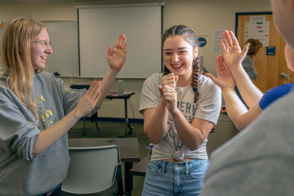 American Sign Language students laugh and practice signing together during a classroom activity.