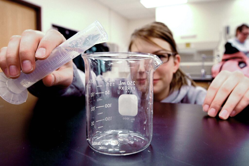 Student pours a liquid into a beaker while conducting a chemistry experiment.