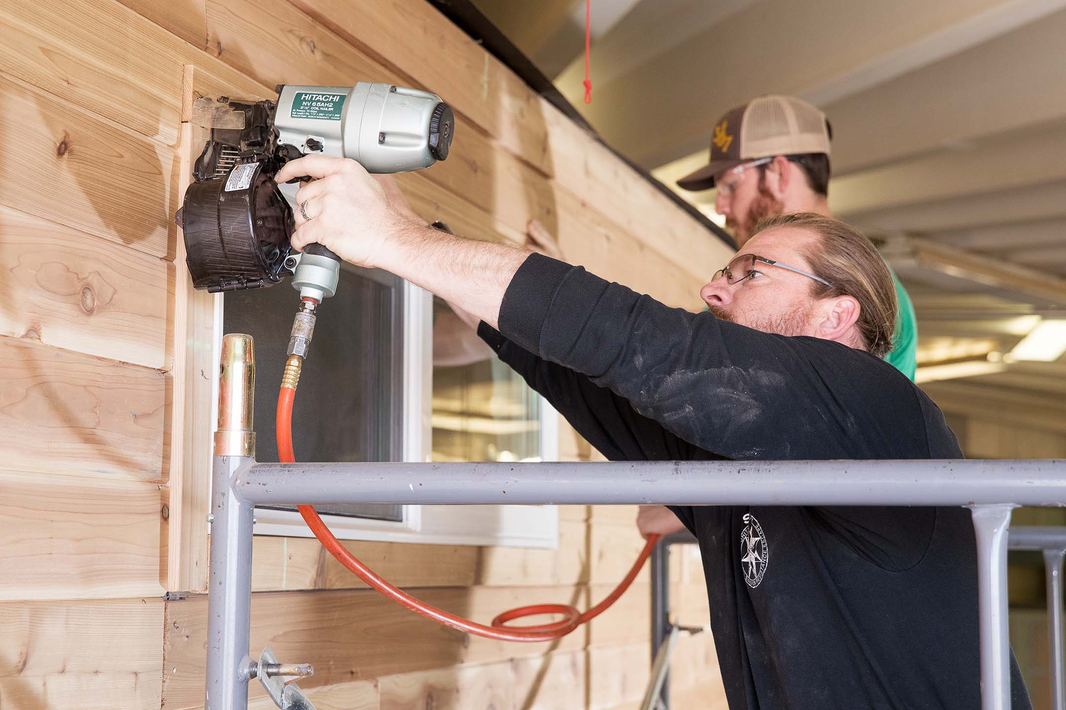 Students install exterior siding with a pneumatic nail gun during hands-on construction training.