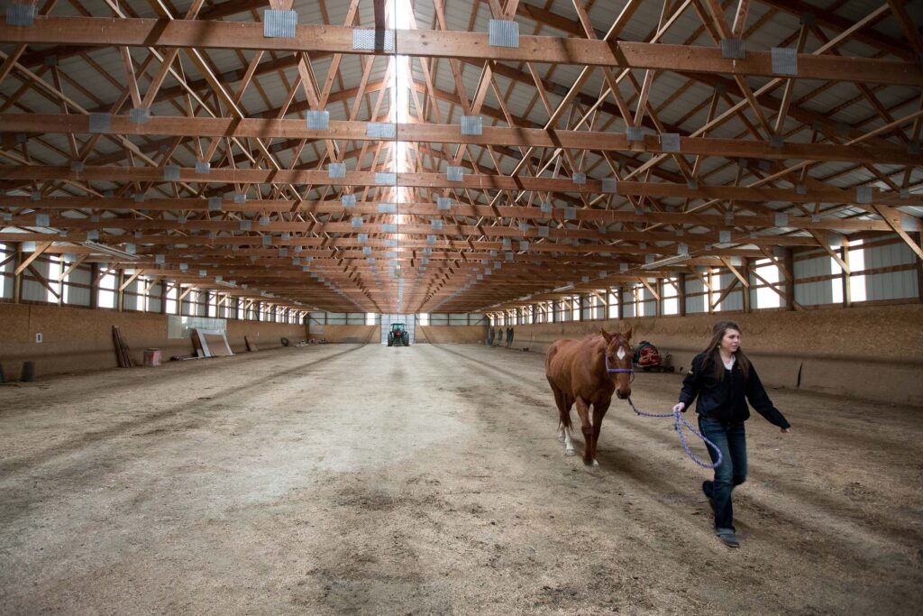 Student leads a horse through a large indoor riding arena used for hands-on ranch management training.