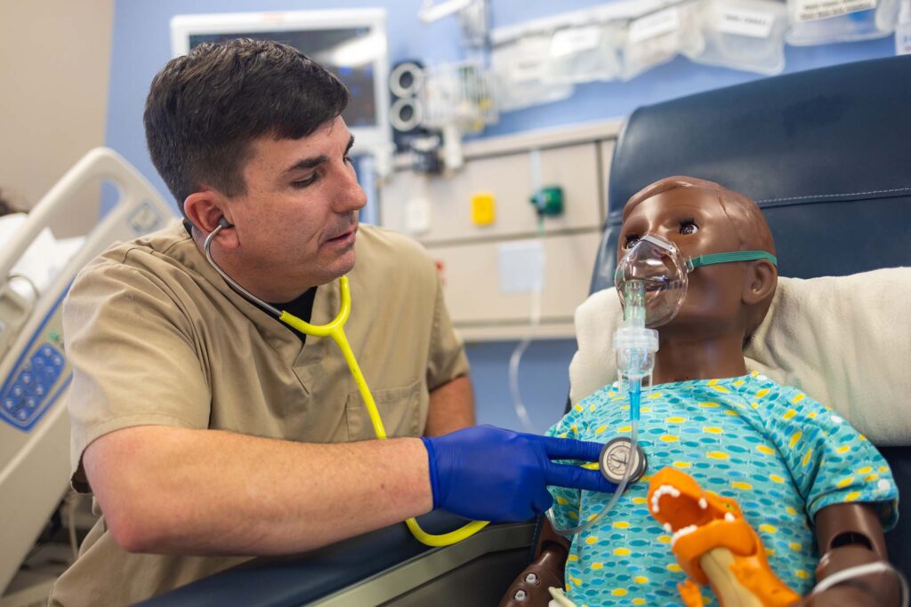Respiratory therapy student assesses a pediatric patient simulator using a stethoscope during a clinical simulation.