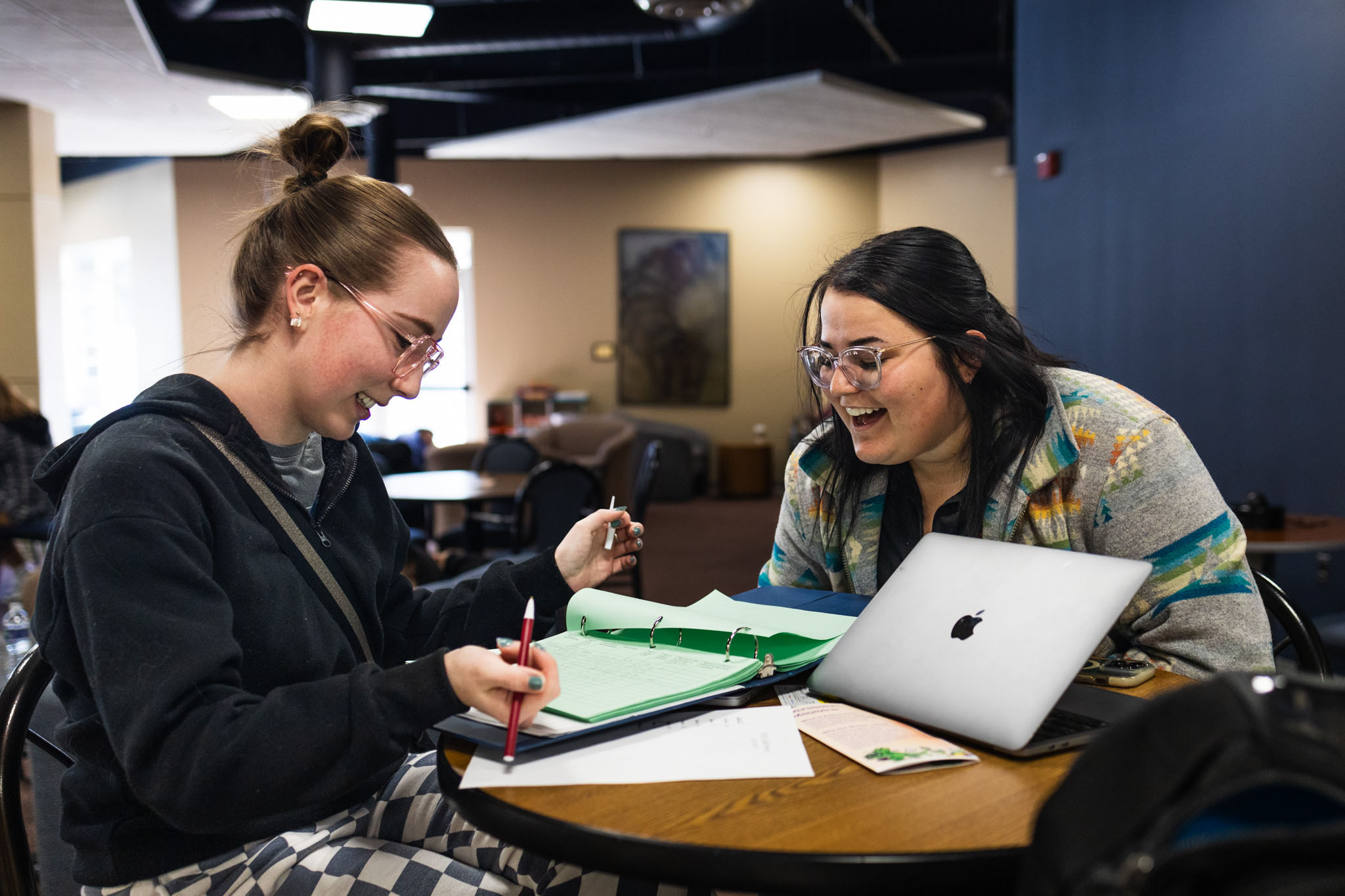 student-marketing-photo-34 Two students smiling and reviewing coursework together at a table with a laptop and open binder as they choose a major.