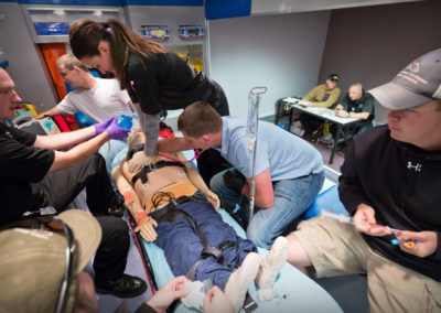 Students work through a scenario of trying to revive a patient with a dummy in the back of a mock paramedic van.