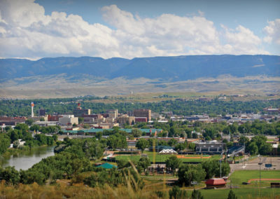 A city with a river through it sits below a small mountain range with blue skies and clouds overhead.