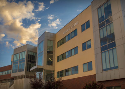 exterior of a three-story building with lots of windows and a blue sky with clouds behind it.