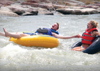 Two students on inner tubes laugh as they get splashed while floating down the river