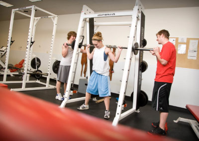Two students spot a third student using a squat rack.