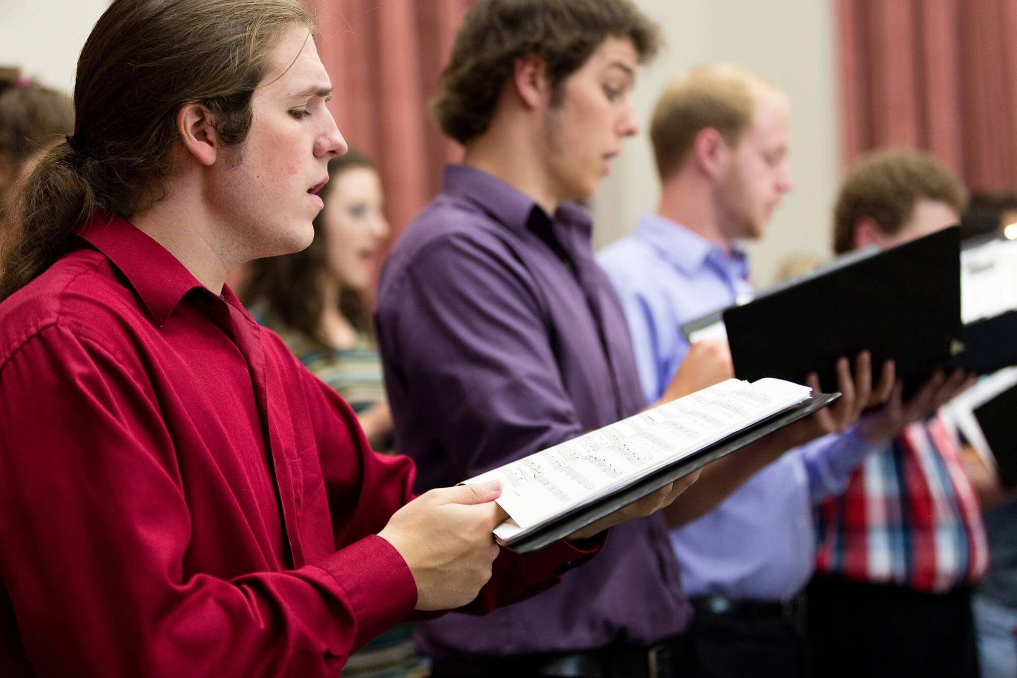 Photo of two male students singing while they read sheet music.