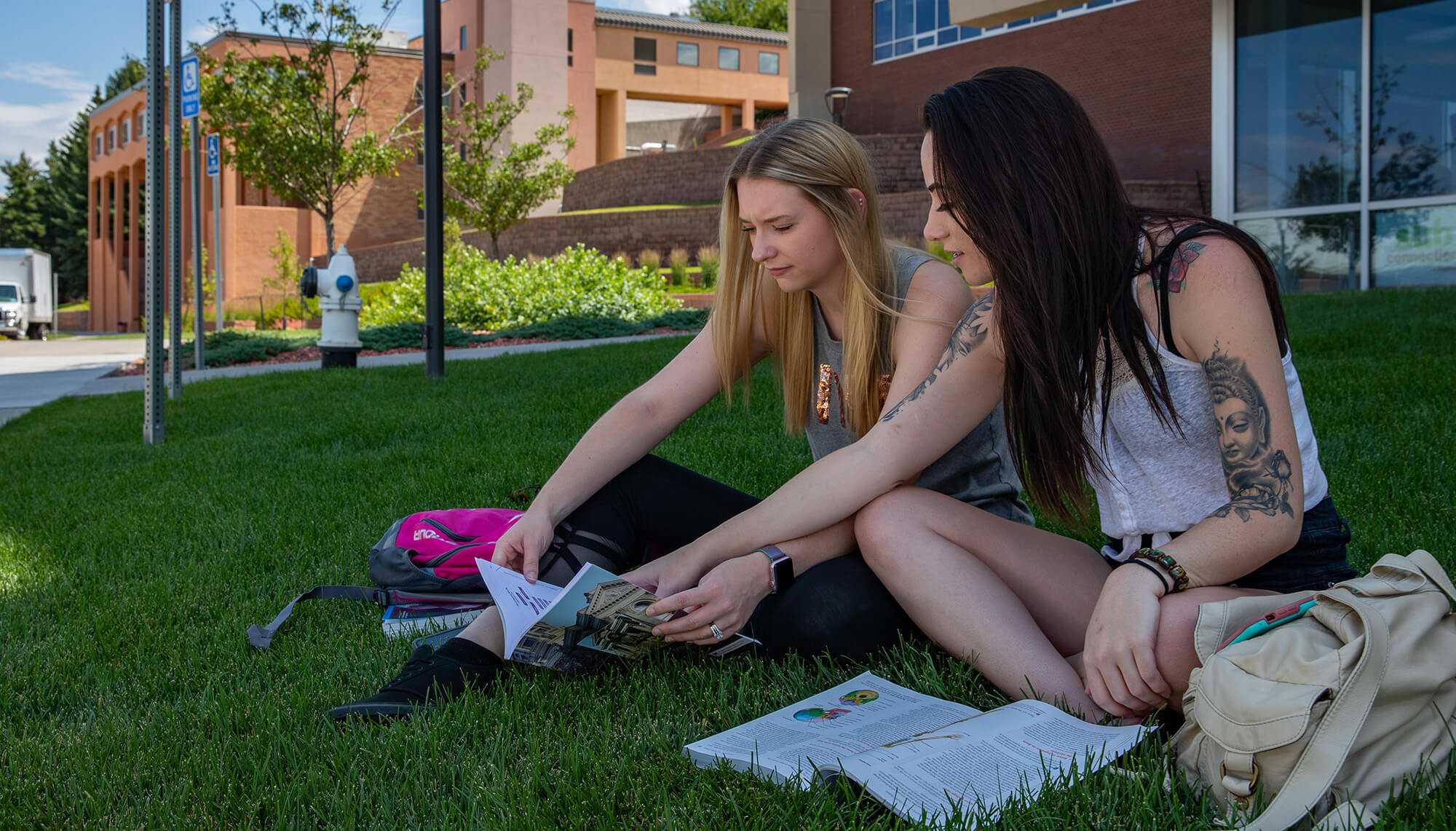 two female students sitting on the grass on campus studying with two textbooks